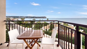 A balcony with a table and chairs, overlooking a coastal view with buildings and a clear sky.