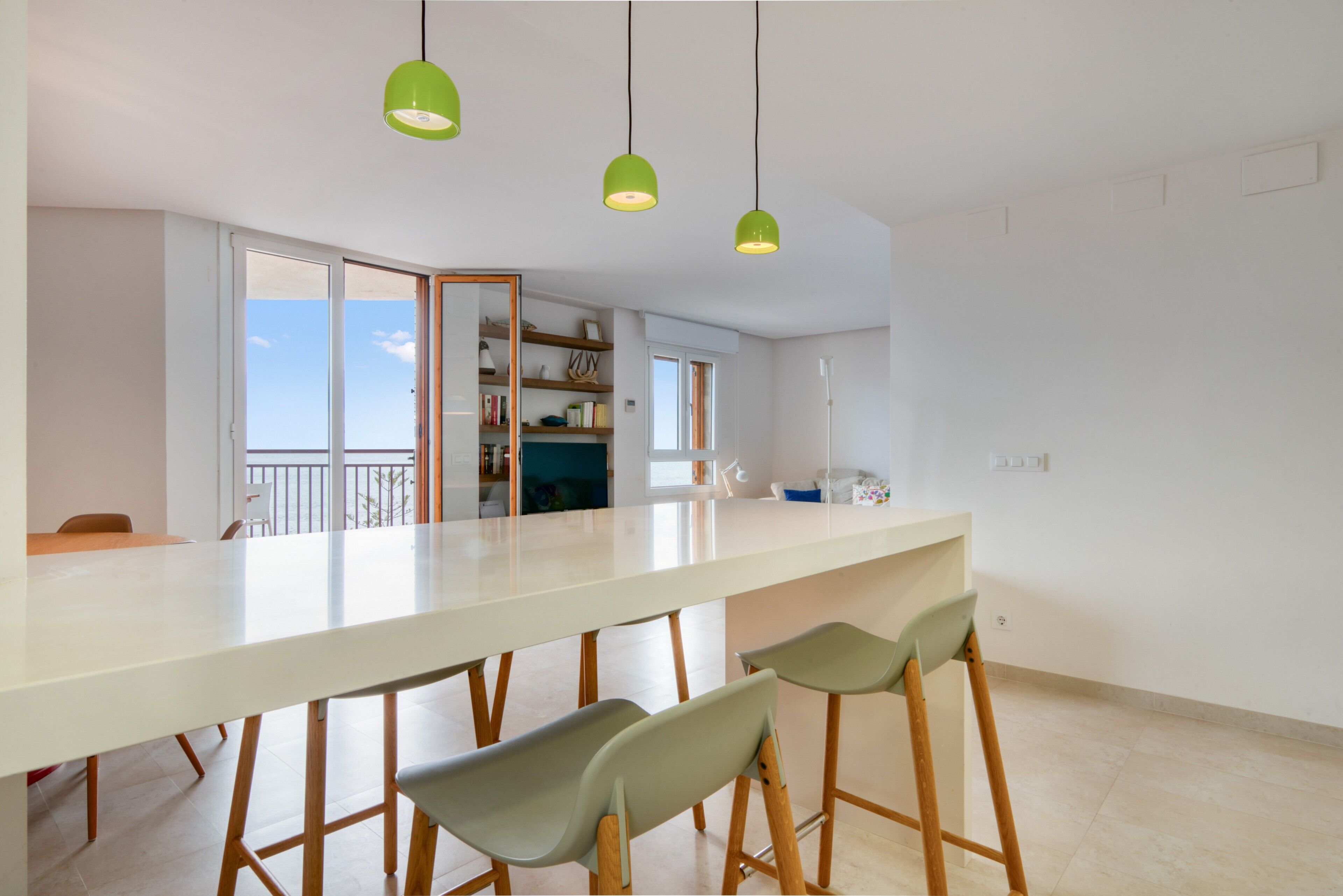 A modern kitchen with a white countertop, green pendant lights, and wooden stools.