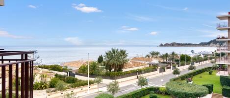A coastal view with a road, greenery, and a building with balconies.