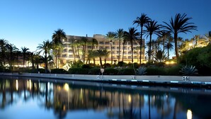 A hotel with a pool, palm trees, and a well-lit building facade.