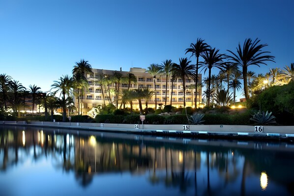 Un hotel con piscina, palmeras y una fachada de edificio bien iluminada.