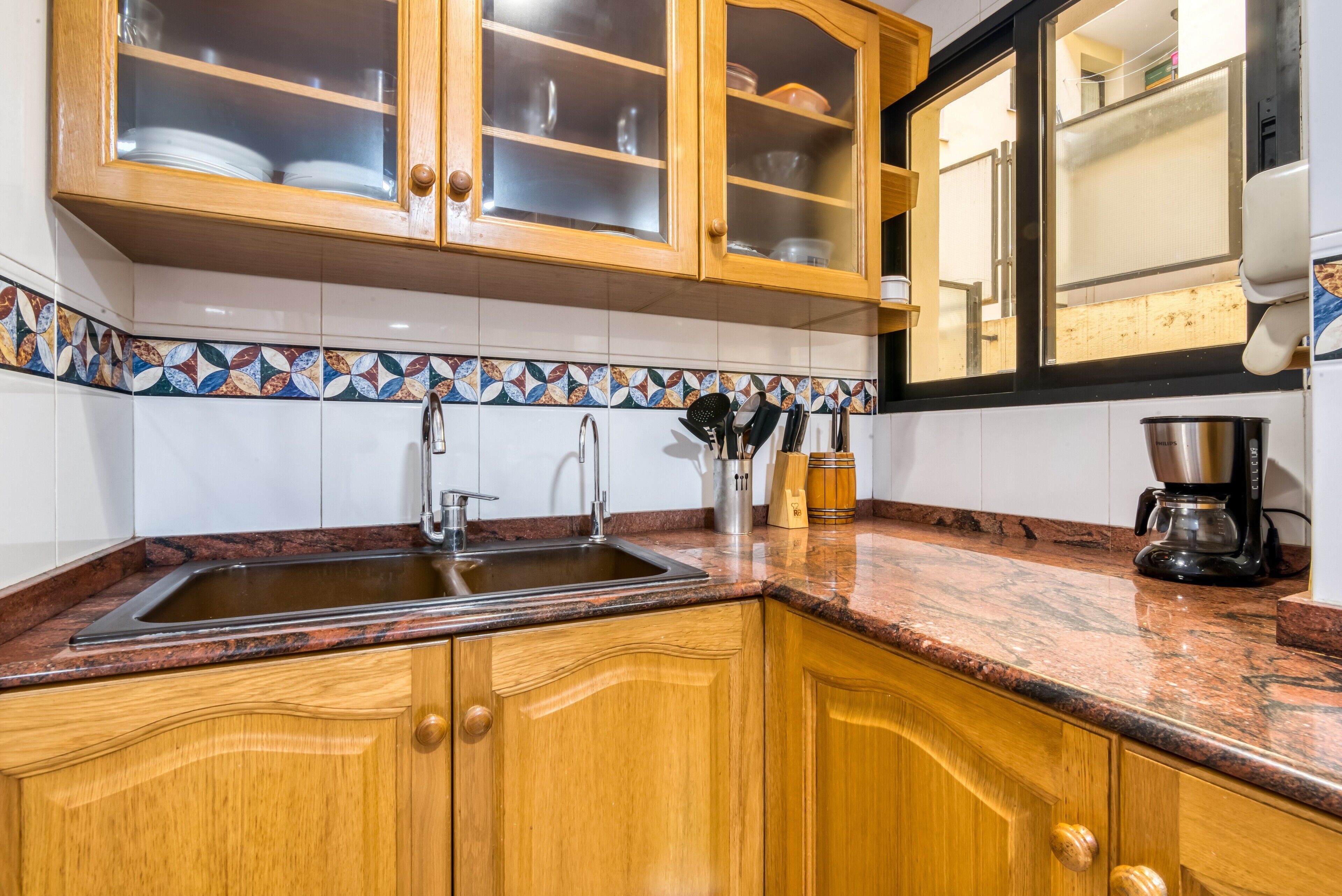 Una cocina con armarios de madera, un lavamanos de acero inoxidable y una cafetera.