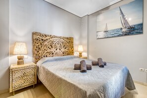 A neatly made bed with a quilted bedspread, two bedside lamps, a decorative headboard, and a framed picture of a sailboat on the wall.