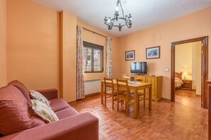 Uma sala de estar com sofá, mesa de jantar, cadeiras, televisão e uma janela com cortinas.