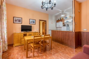 A dining area with a wooden table and chairs, a television, and a kitchen area with cabinets and a microwave.