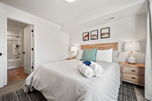 Een hotelkamer met een groot bed, twee nachtkastjes, een houten hoofdbord en een deur naar een badkamer.