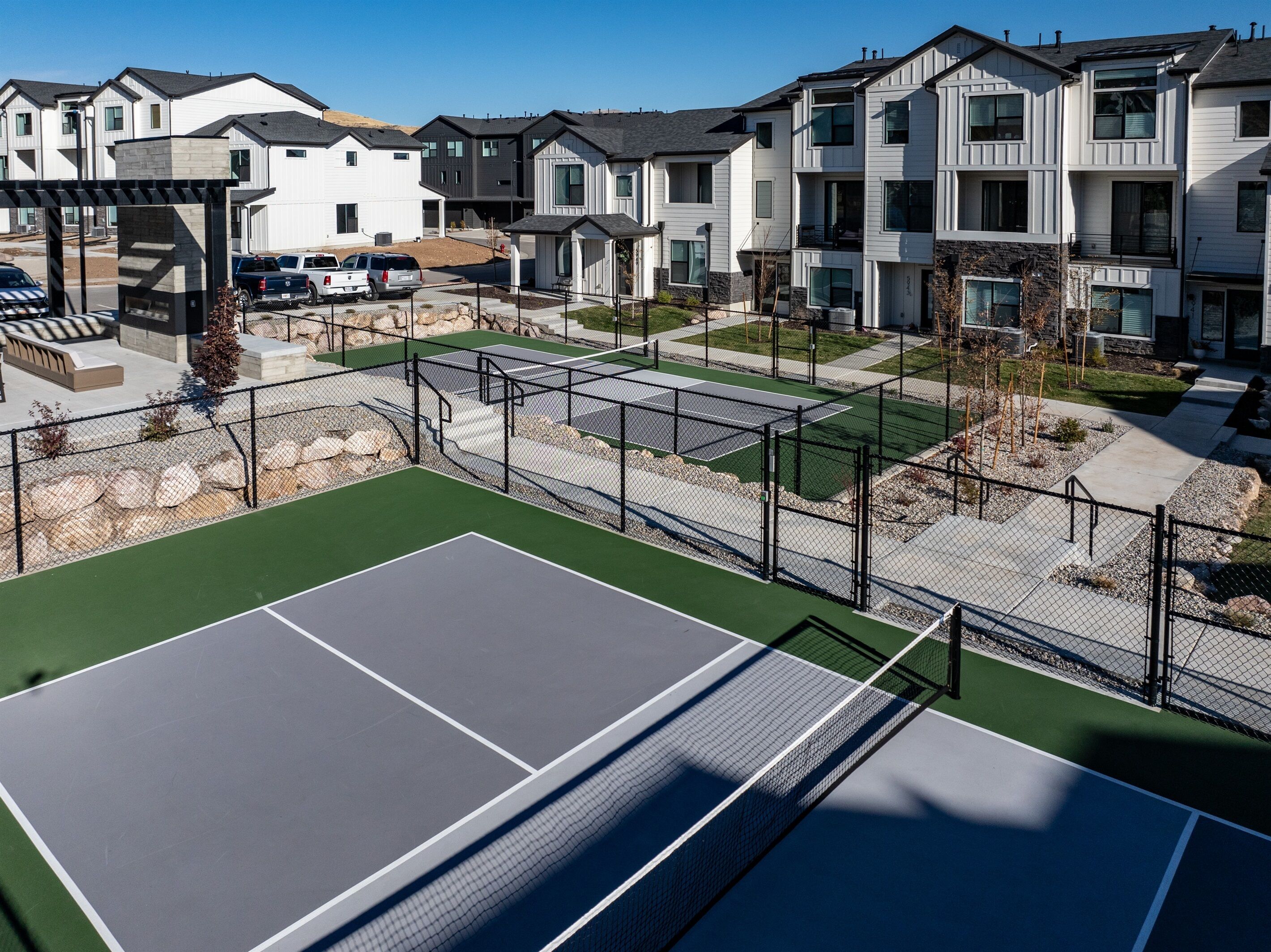 En tennisbane omgivet af høje boligbygninger med en parkeringsplads foran.