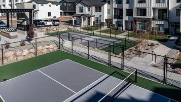 En tennisbane omgivet af høje boligbygninger med en parkeringsplads foran.