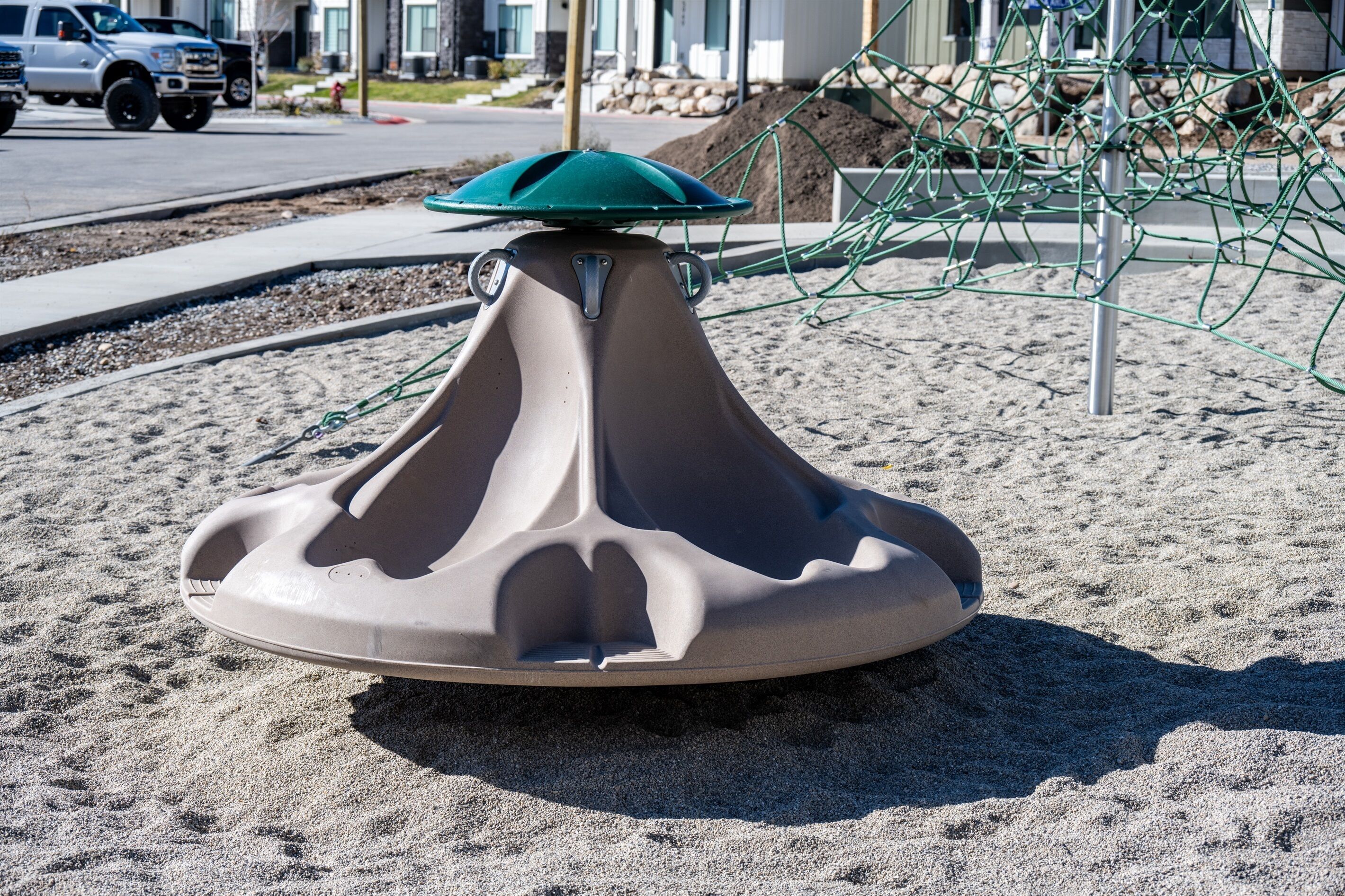 A sand play area with a green top and a beige base, surrounded by a playground structure.