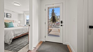 Une chambre d’hôtel avec un lit, une table de chevet, une lampe et une vue sur la rue, visible à travers une porte vitrée.
