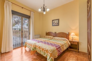 A bedroom with a bed, a nightstand, a lamp, a picture on the wall, and a view through a sliding door.