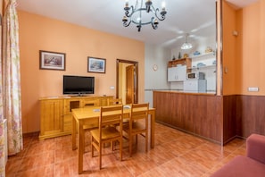 A dining area with a wooden table and chairs, a television, and a kitchen in the background.