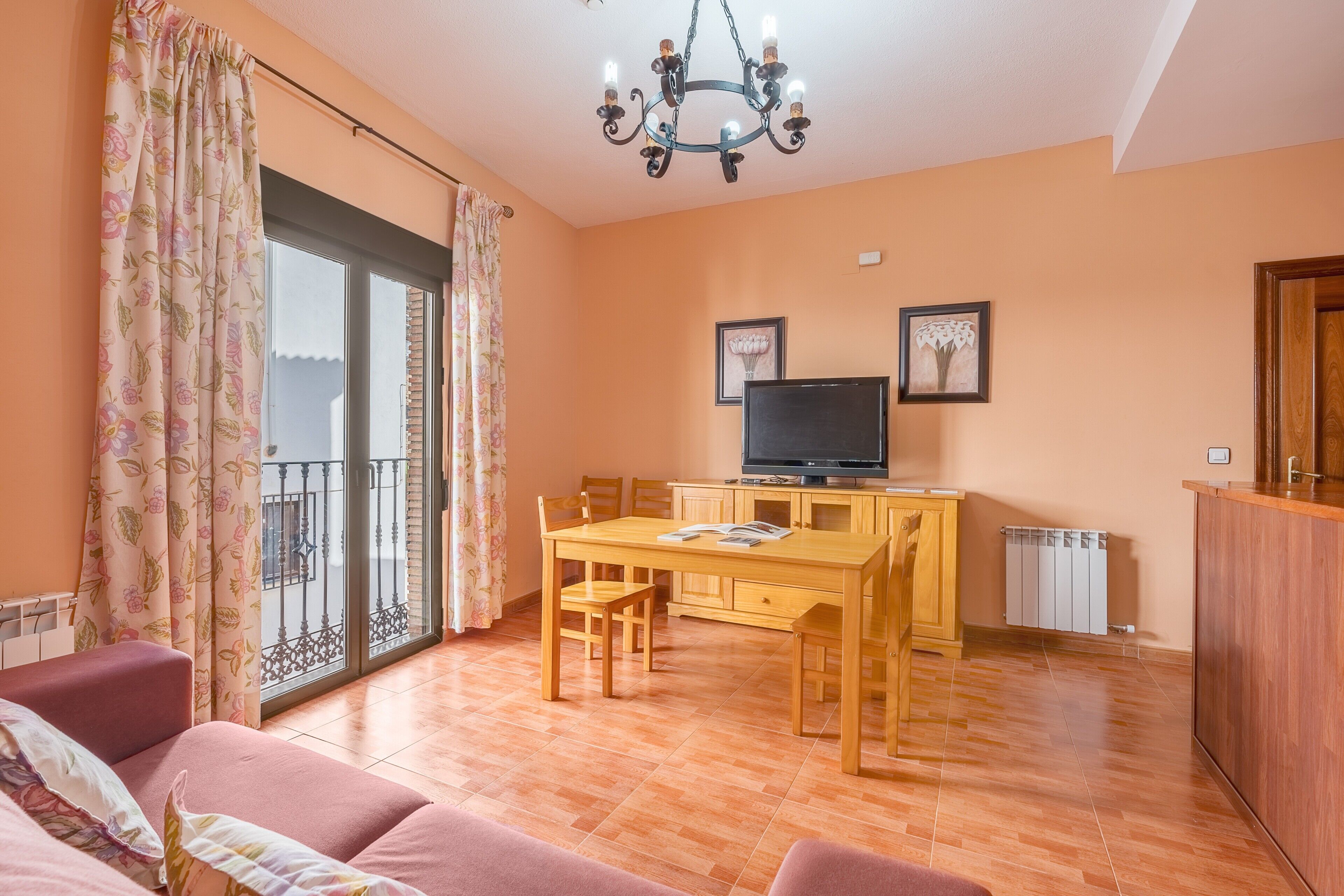 A living room with a sofa, a dining table, a TV, and a balcony with curtains.