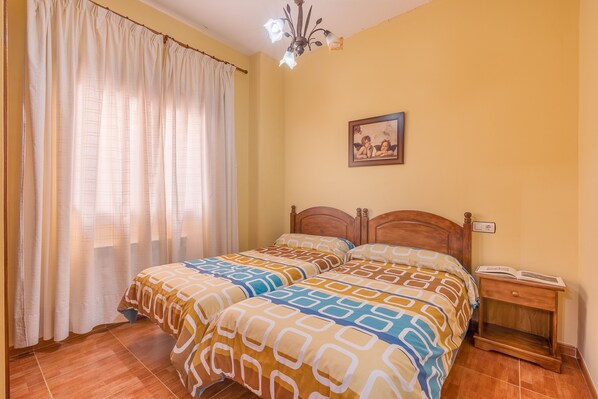 A bedroom with a bed, curtains, a nightstand, and a wall-mounted picture.