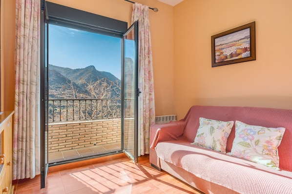 A room with a balcony, a sofa with floral cushions, and a framed picture on the wall.