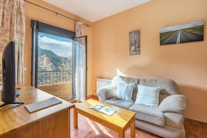 A living room with a sofa, a coffee table, a TV, and a window with a view of mountains.