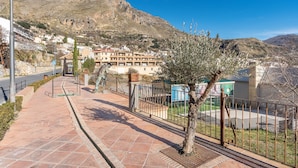 A paved walkway with a metal fence, a street lamp, and a view of a hillside with buildings. - Apartment 'Apartamento De 1 A 2 Personas' with Balcony and Wi-Fi (Güejar Sierra)
