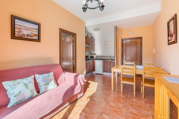 A living room with a sofa, a dining table, and a kitchen in the background.