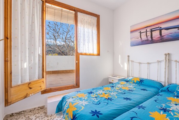 A bedroom with a bed, a window with curtains, a bedside table, and a wall-mounted picture.