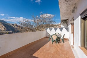 Un balcon avec une table et des chaises, une vue sur les montagnes et un bâtiment à la façade blanche et au design géométrique.
