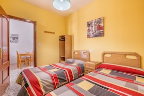 Une chambre avec deux lits, une table de chevet en bois, une armoire en bois, une petite table avec des chaises et un tableau accroché au mur.