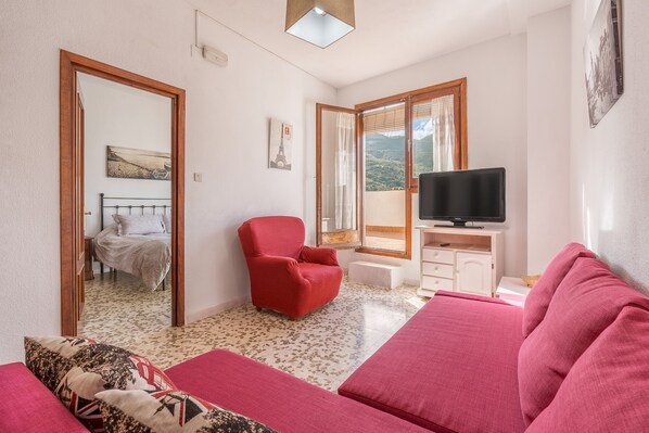 A room with a bed, a red armchair, a TV, and a balcony with a view.