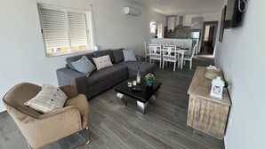 Un salon moderne avec un canapé gris, un fauteuil marron et un coin repas comprenant des chaises blanches et une table.