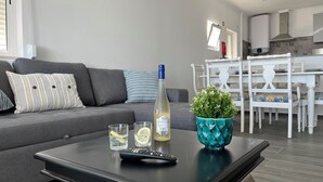 Un salon moderne avec un canapé gris, une table basse noire, une bouteille d’eau, des verres et une télécommande.