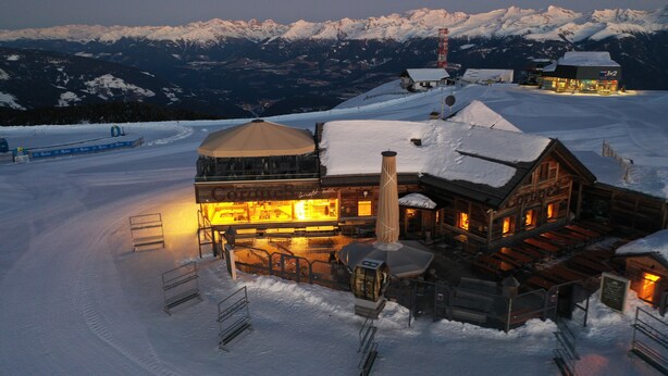 Ein schneebedecktes Bergresort mit einer Holzhütte, einer überdachten Außenbestuhlung und einer Seilbahn.