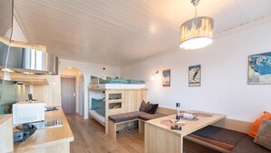 Ein kompakter, moderner Raum mit Küchenzeile, Etagenbett, Essbereich und Sitzecke.