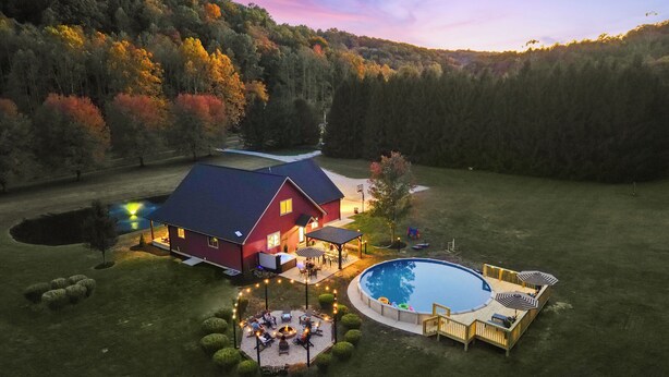 Une grande maison avec une piscine, entourée d’une pelouse bien entretenue et d’une zone boisée.