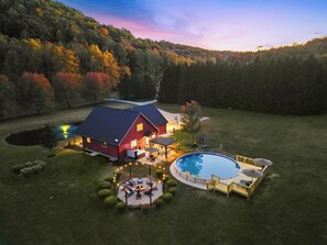 Une grande maison avec une piscine, entourée d’une pelouse bien entretenue et d’une zone boisée.