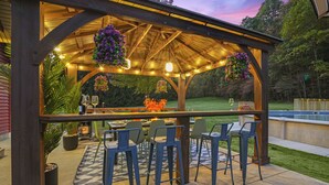 Une terrasse extérieure dotée d’une pergola en bois, d’un espace bar et de coins salon.