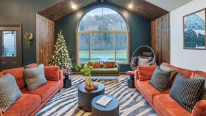 Un salon chaleureux avec deux canapés, un sapin de Noël et une grande fenêtre donnant sur une forêt.