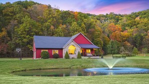 Un bâtiment de couleur rouge, de style grange, avec un étang devant, entouré d’un paysage verdoyant et luxuriant.