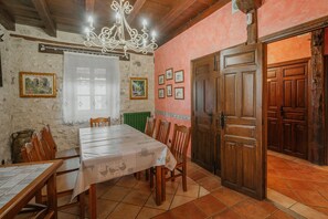 A dining area with a table set for four, wooden chairs, a chandelier, and a door with a rustic design.