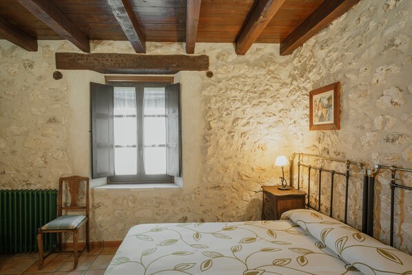 A rustic room with a bed, a chair, a window, and a picture on the wall.