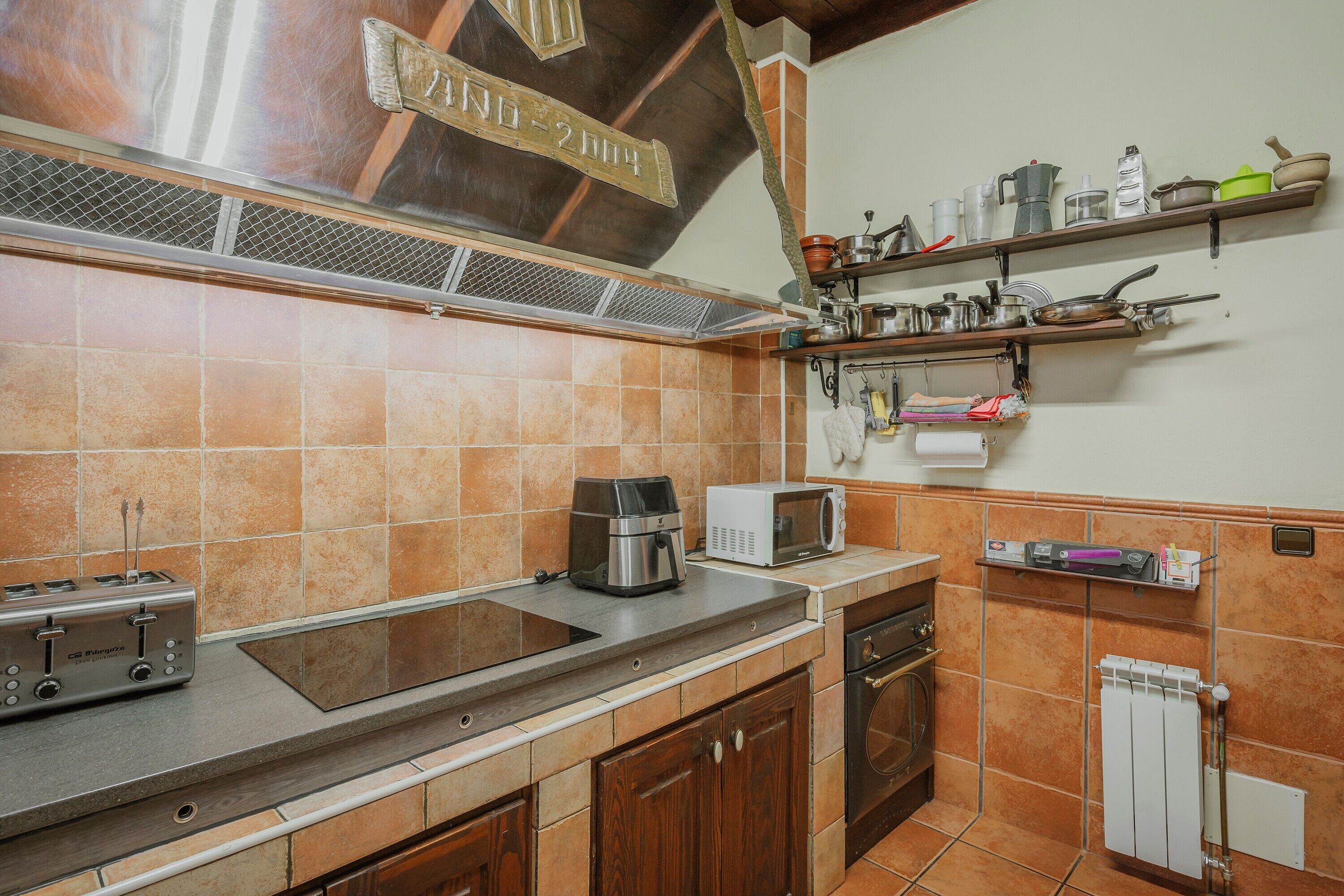 Een keuken met een fornuis, magnetron, broodrooster en diverse keukengerei op planken.