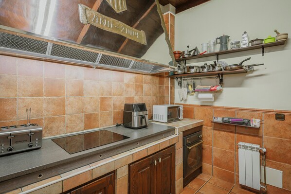 A kitchen with a stove, microwave, toaster, and various kitchen utensils on shelves.