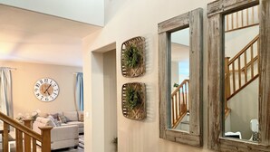 Un salon avec un escalier en bois, une horloge et deux miroirs fixés au mur.