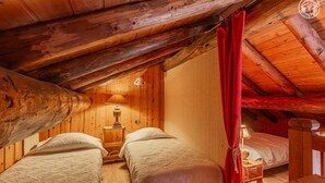 Une pièce chaleureuse, aménagée dans un chalet en bois, avec deux lits, un rideau rouge et une petite table sur laquelle se trouve une lampe.