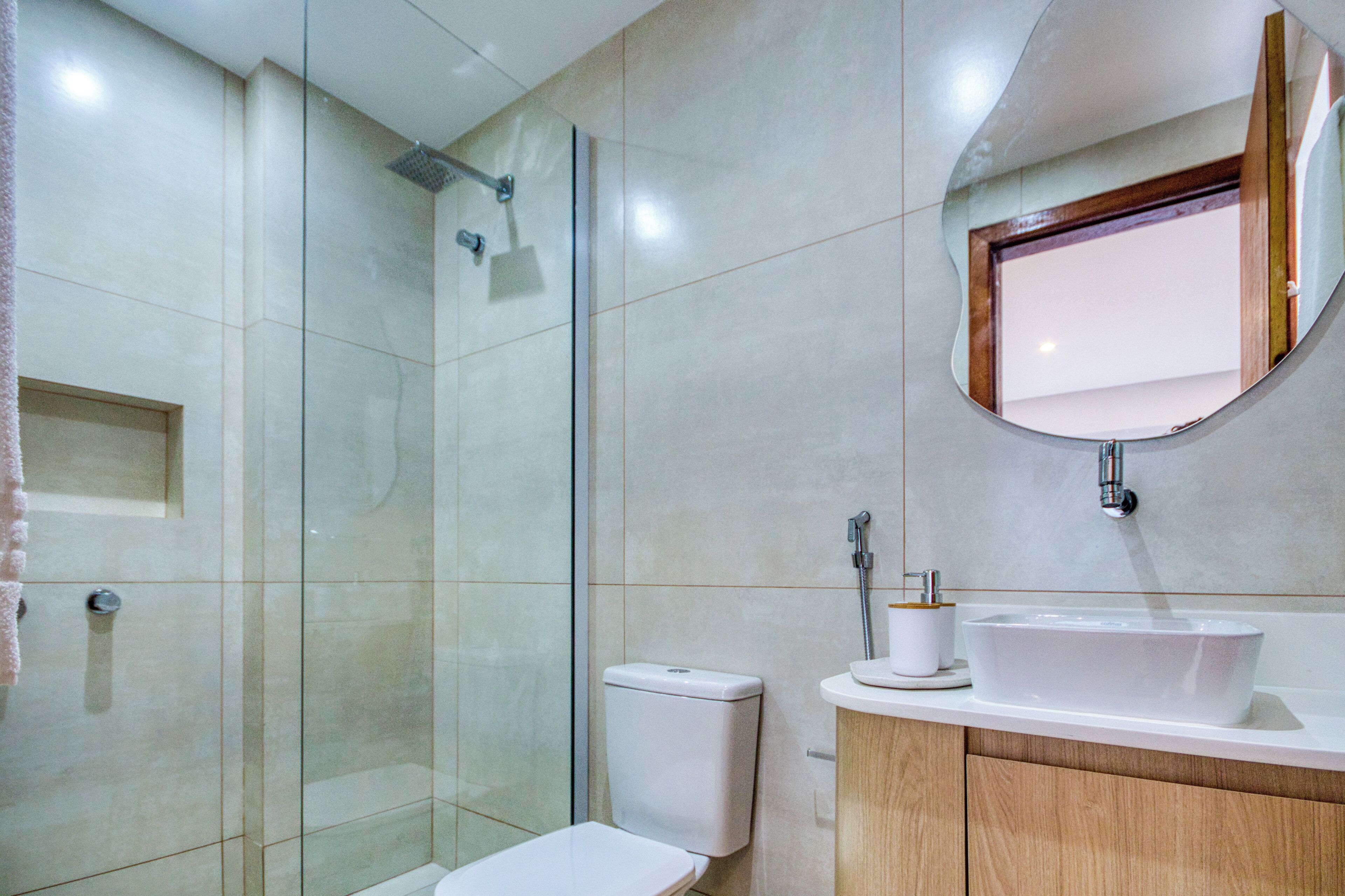 Een moderne badkamer met een glazen douchecabine, een toilet, een wastafel met spiegel en een handdoekrek.
