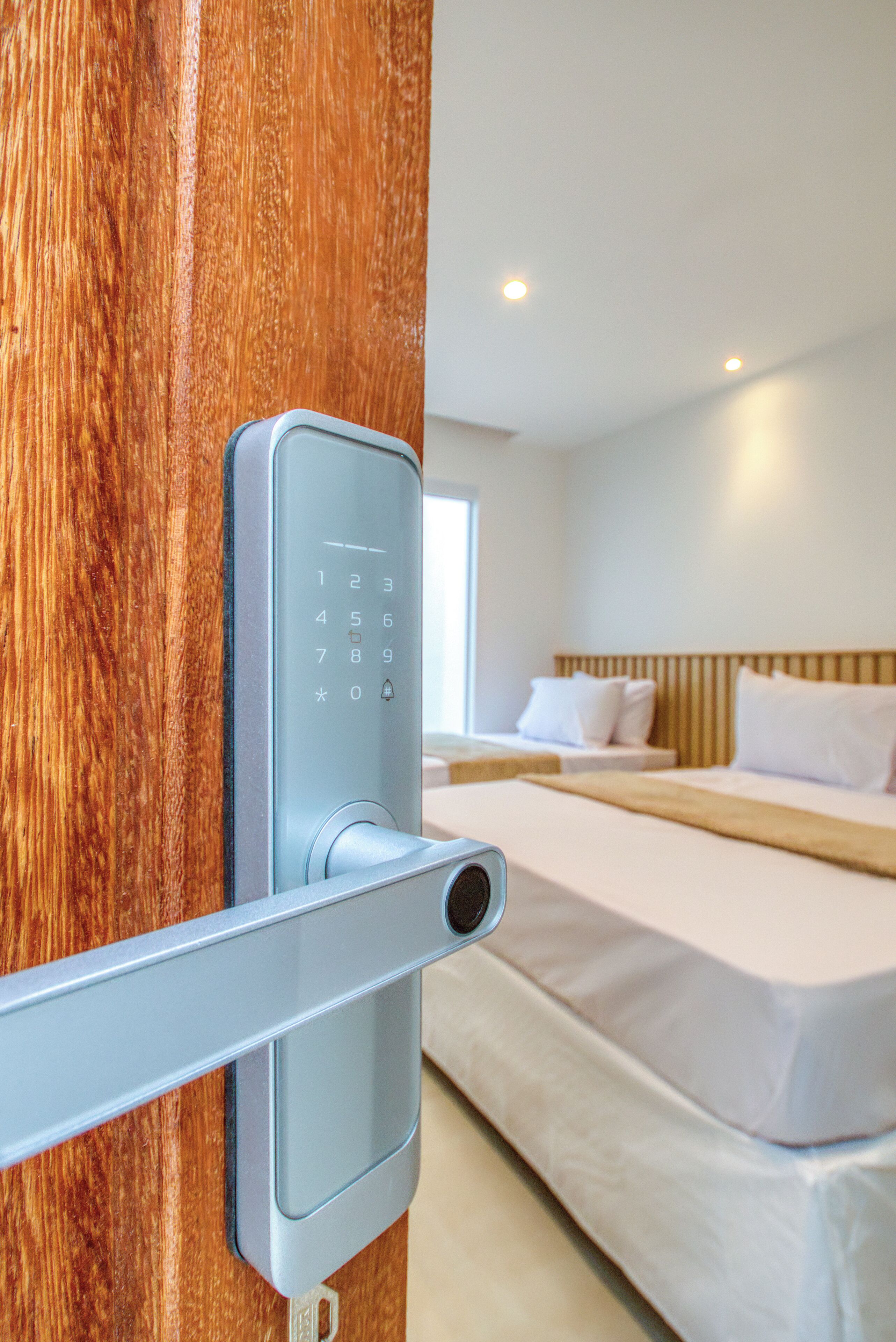 Una habitación de hotel moderna con cerradura digital en la puerta, una cama bien hecha y un cabecero de madera.