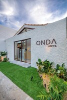 Un edificio moderno con el letrero "ONDA LOFTS" en la fachada, que presenta una puerta de cristal grande y un césped bien cuidado con diversas plantas.