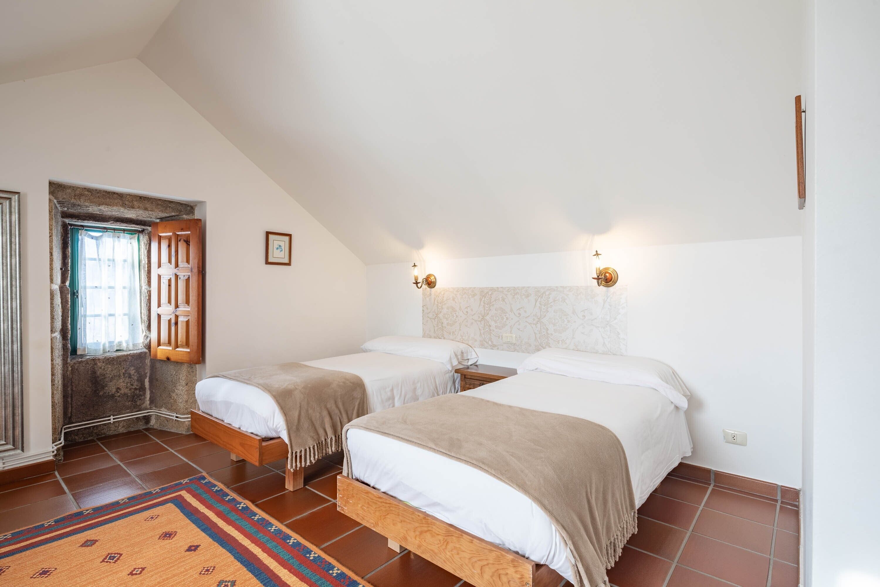 A bedroom with two beds, a wooden door, a patterned rug, and a light fixture on the wall.
