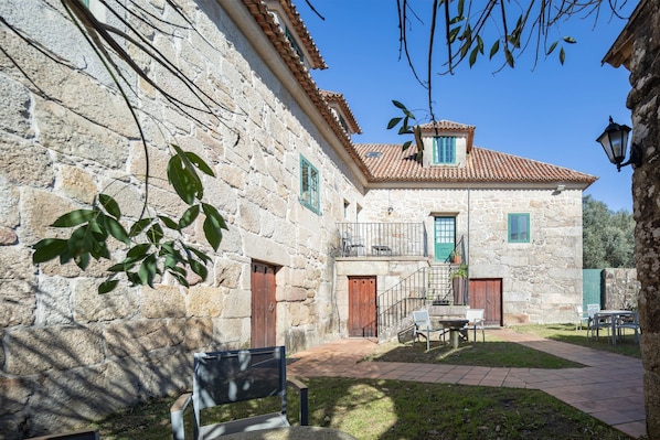 A stone building with a tiled roof, a balcony, and a small outdoor seating area.