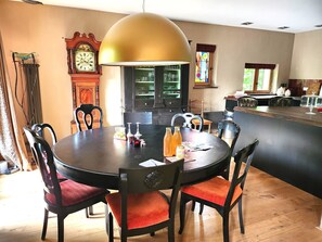 A dining area with a round table, chairs, a large pendant light, a clock, and a bar area with a refrigerator.