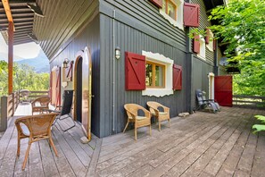 A wooden deck with wicker chairs, a grill, and a view of the mountains.