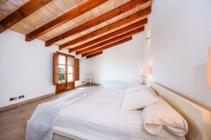 A bedroom with a large bed, wooden ceiling beams, a small bedside table, and a nightstand with a lamp. - Holiday Home 'Pina' with Mountain View, Private Pool and Wi-Fi (Pina)