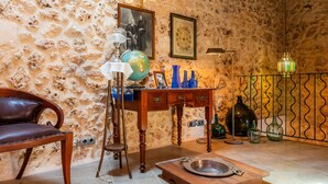 A room with a stone wall, a wooden table with a globe, a framed photograph, and a metal railing with hanging lights.